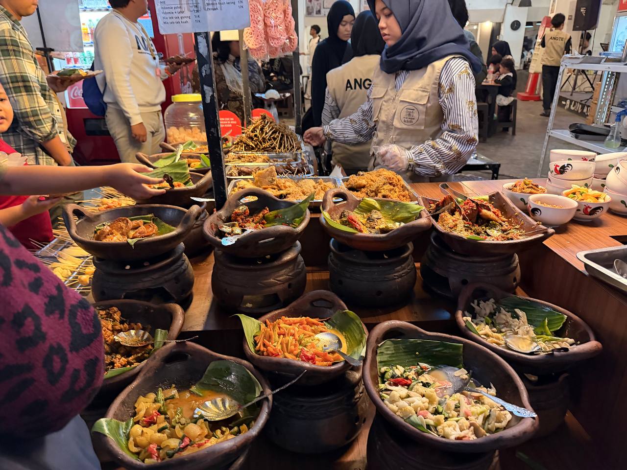 Bandung street food buffet stall at Jalan Braga — clay pots of lauk pauk, local vendor serving customers at night