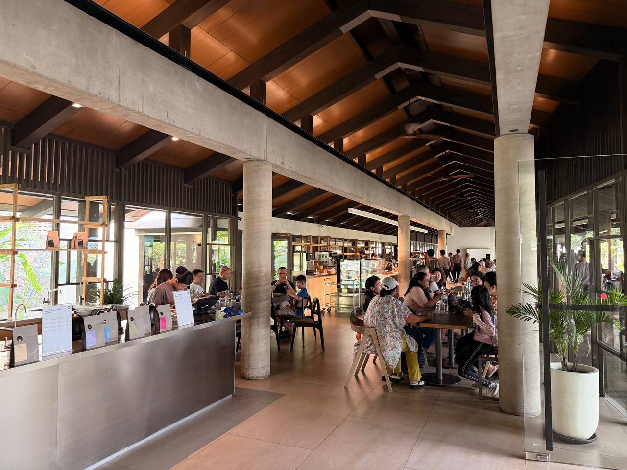 Wheels Coffee Roasters interior — concrete pillars, exposed wood beam ceiling, customers at tables, Dago Bandung