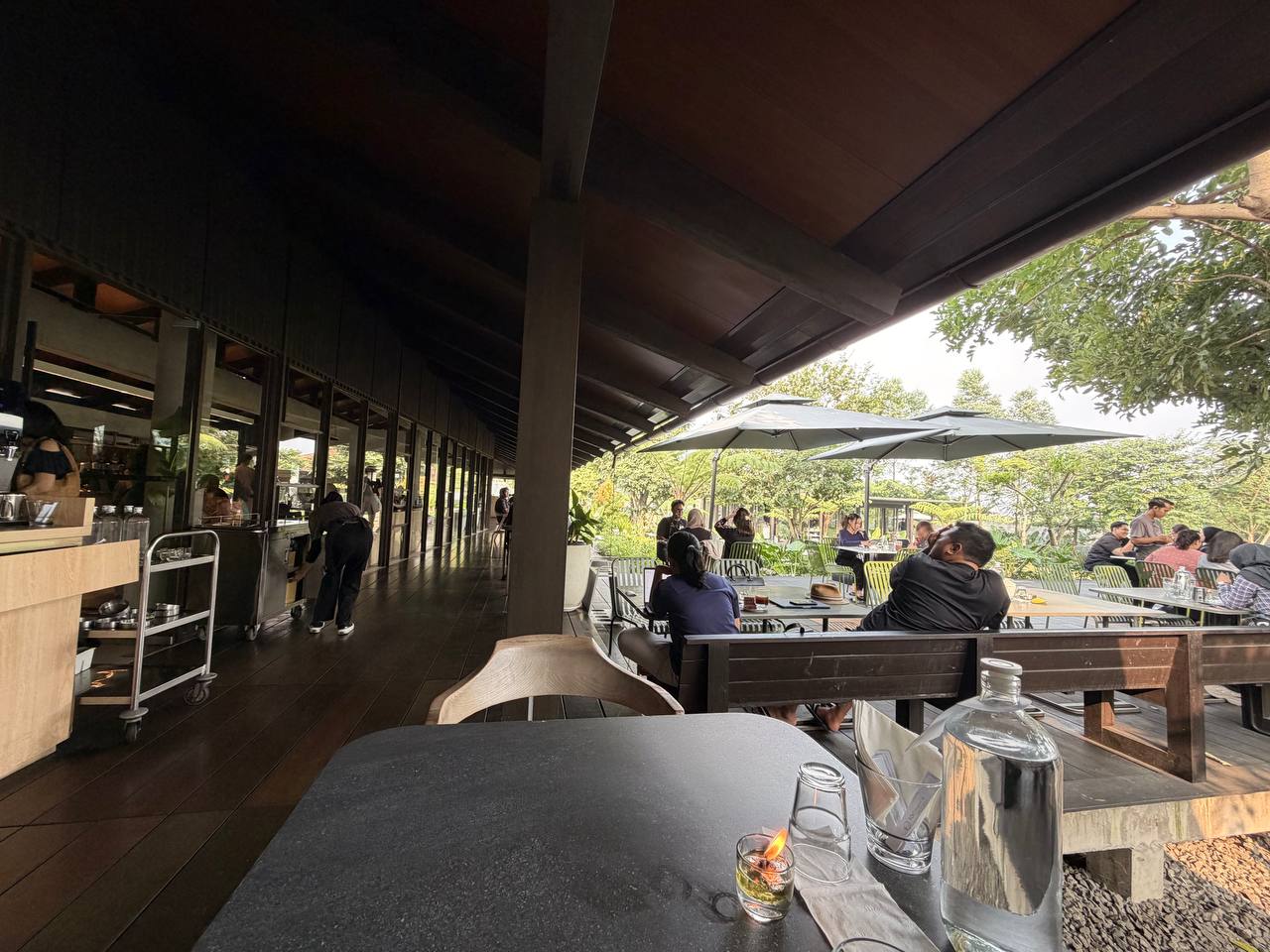 Wheels Coffee Roasters outdoor terrace — packed tables under umbrellas surrounded by greenery, Dago Bandung