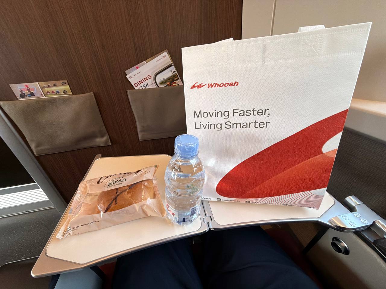 Whoosh first class amenities — branded tote bag, bottled water, and complimentary bread