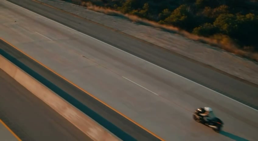 Aerial drone-style shot of the motorcycle rounding a mountain curve, AI-generated